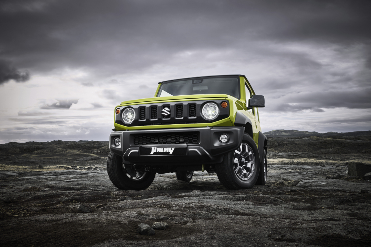 A lime green Suzuki Jimny driving over rocky terrain.